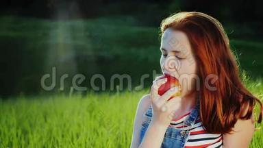 红发少年在野餐时吃<strong>一个</strong>多汁的<strong>红苹果</strong>。 <strong>一个</strong>风景如画的地方-一片绿色的草地，美丽的眩光从